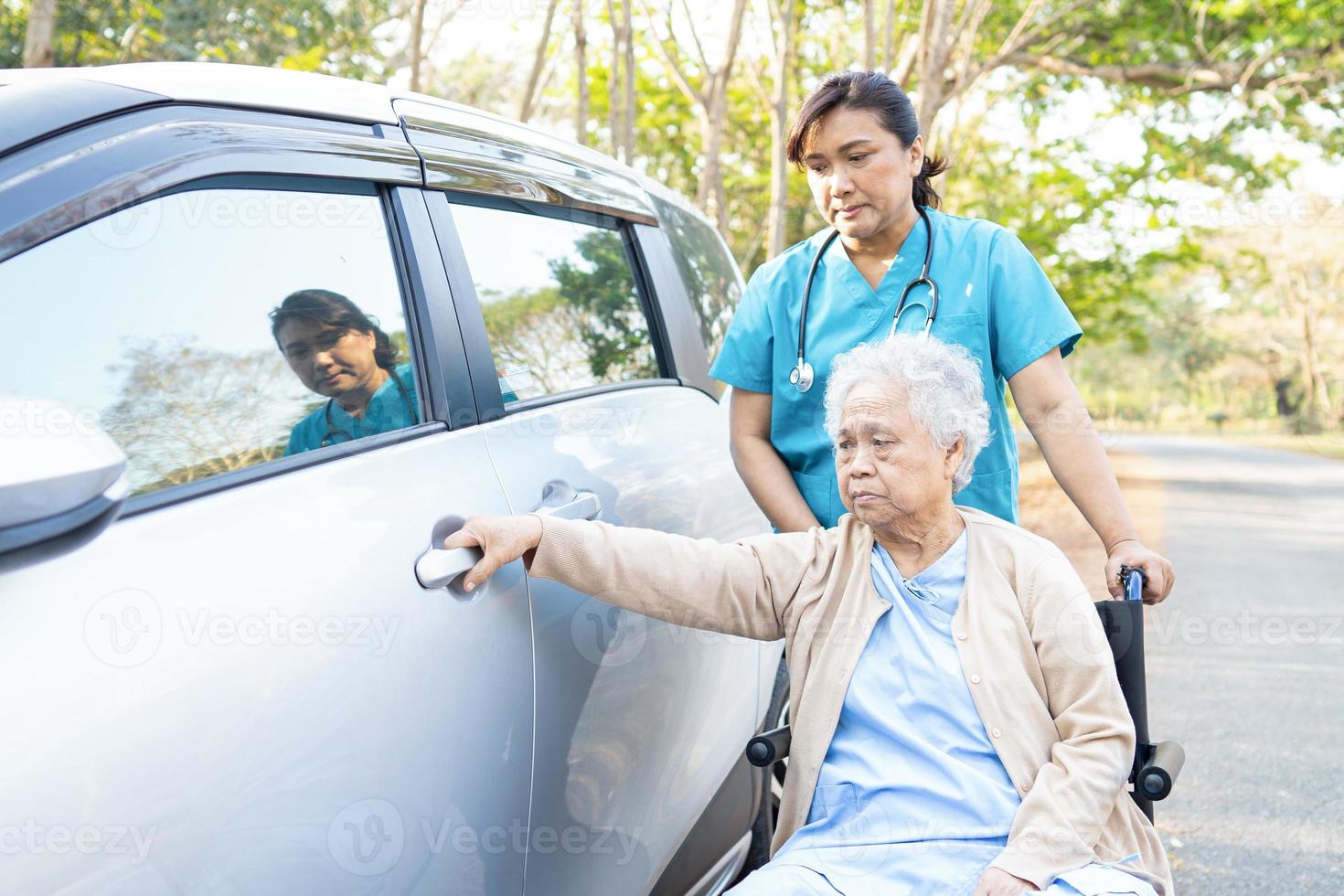 hulp en ondersteuning van aziatische senior vrouw patiënt op rolstoel om naar de auto te gaan foto
