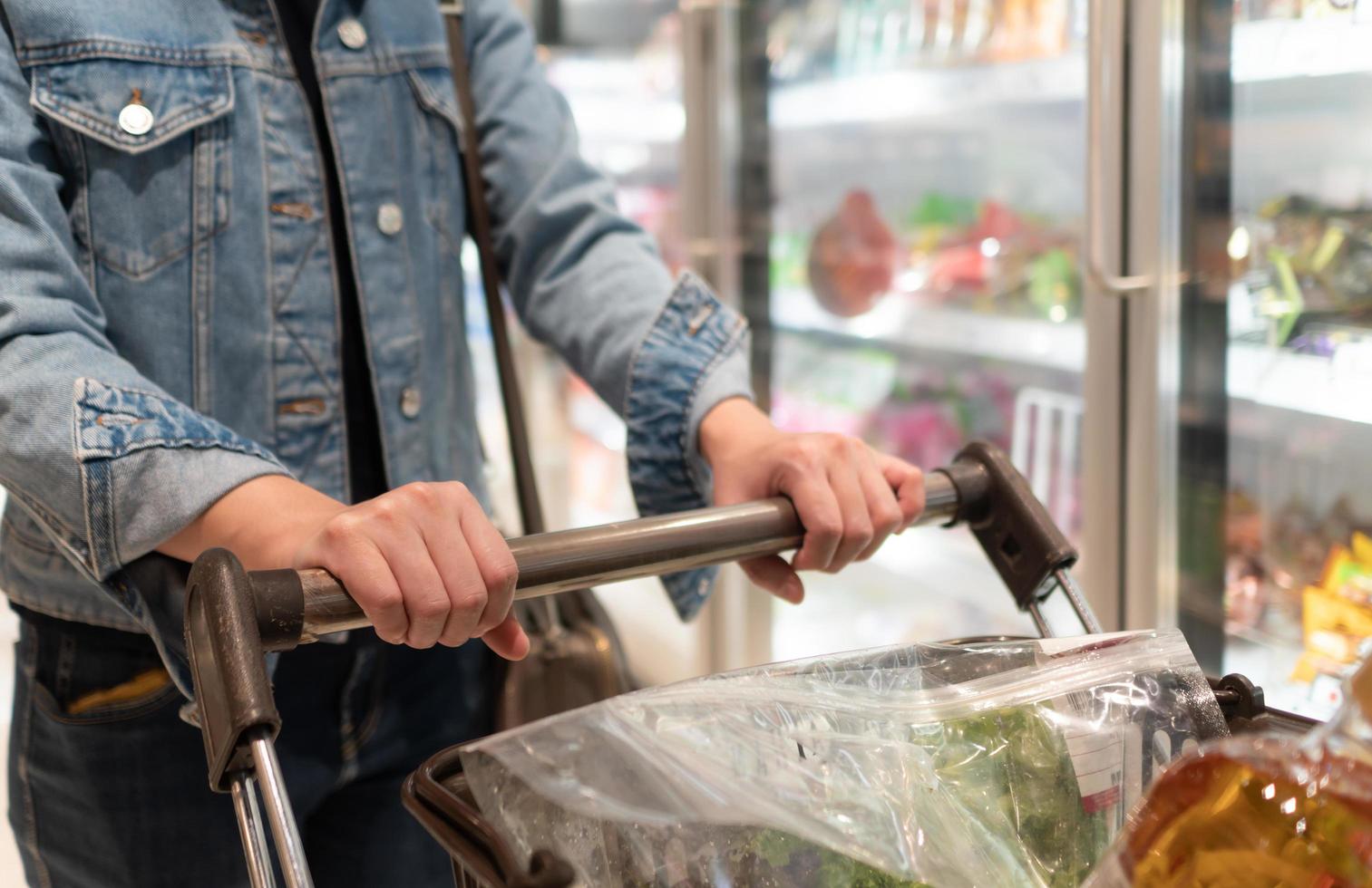 vrouw die winkelwagentje gebruikt om boodschappen in de supermarkt te kopen foto