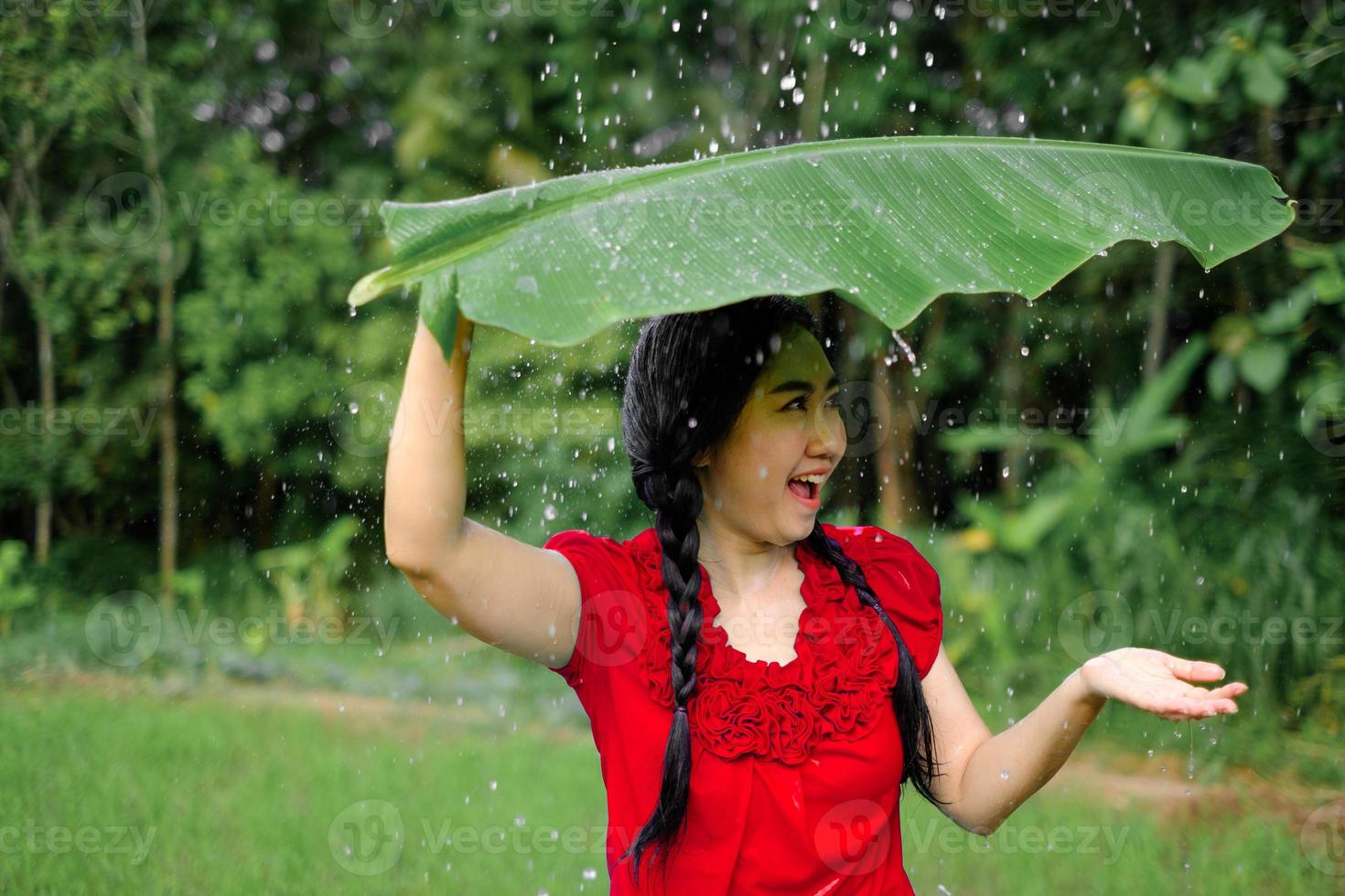 Aziatische vrouw zat onder een bananenblad en zocht beschutting tegen de regen foto