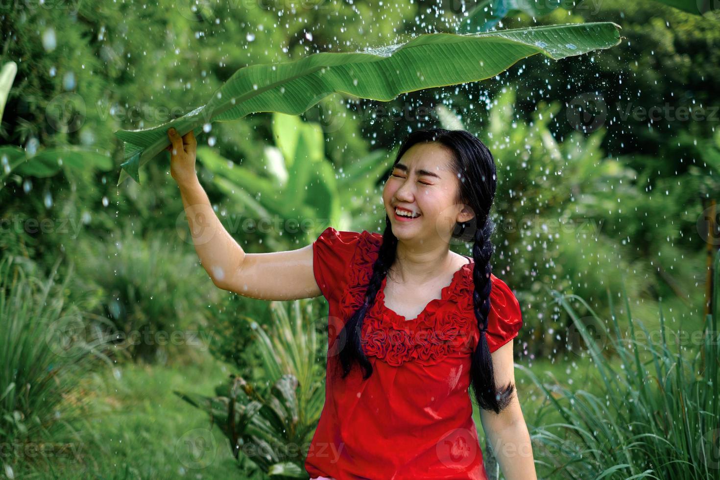 Aziatische vrouw zat onder een bananenblad en zocht beschutting tegen de regen foto