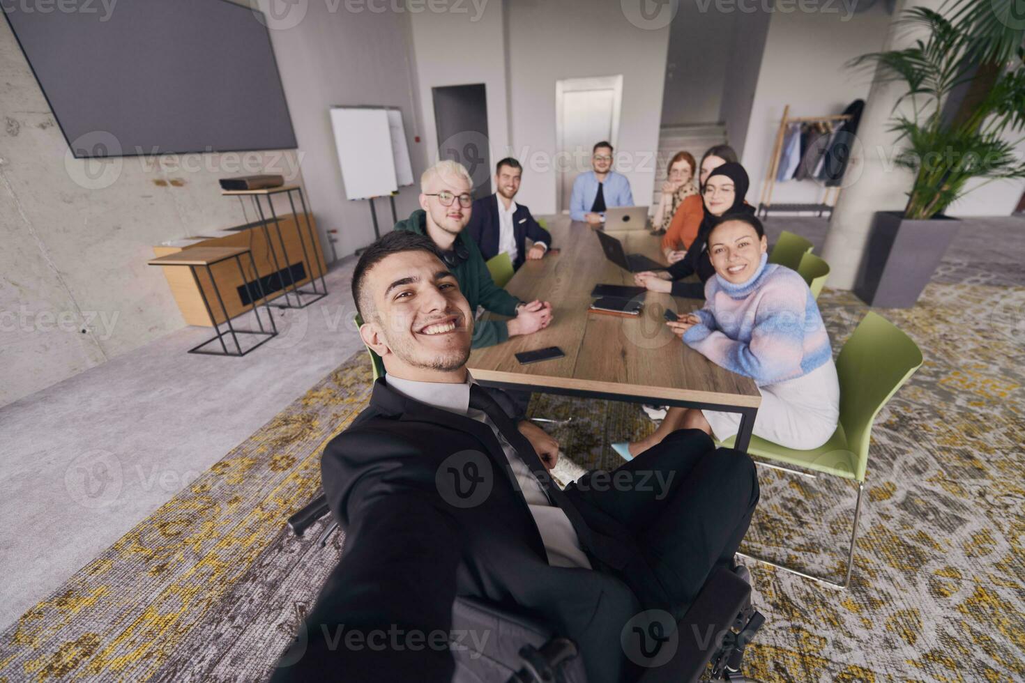 in een modern kantoor, een groep van zakenlieden verzamelt in de omgeving van een tafel gedurende een ontmoeting, vastleggen een moment van kameraadschap en samenspel net zo ze nemen een selfie foto