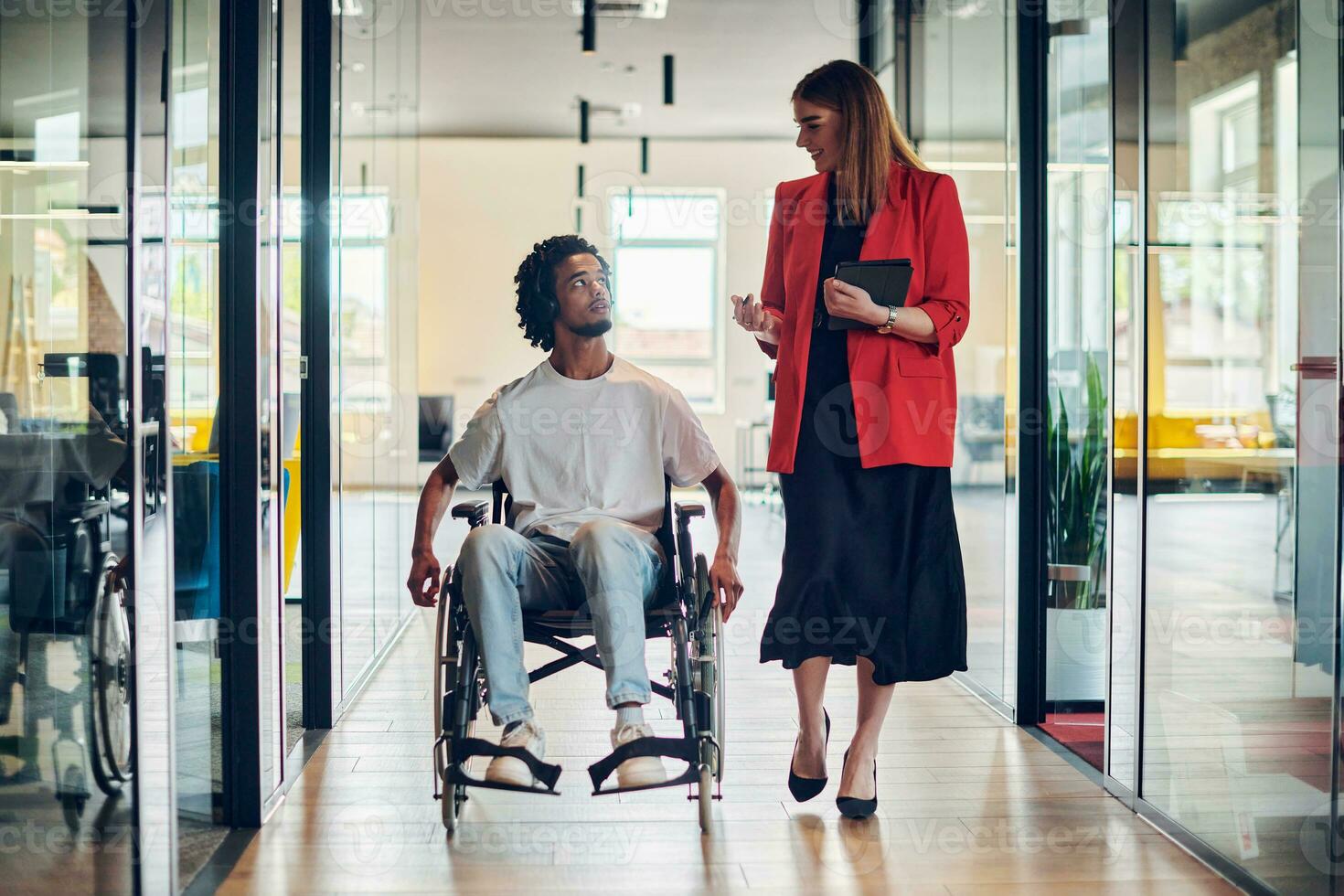 een groep van jong bedrijf mensen in een modern glazen wanden kantoor vangt de essence van verscheidenheid en samenwerking, terwijl twee collega's, inclusief een Afrikaanse Amerikaans zakenman in een rolstoel, reflecteren inclusiviteit en bespreken oplossen bedrijf probleem foto