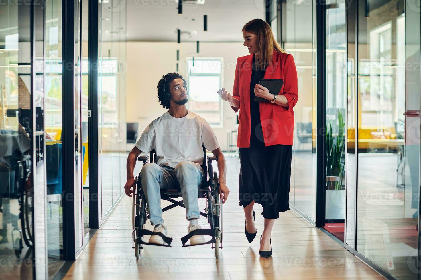 een groep van jong bedrijf mensen in een modern glazen wanden kantoor vangt de essence van verscheidenheid en samenwerking, terwijl twee collega's, inclusief een Afrikaanse Amerikaans zakenman in een rolstoel, reflecteren inclusiviteit en bespreken oplossen bedrijf probleem foto