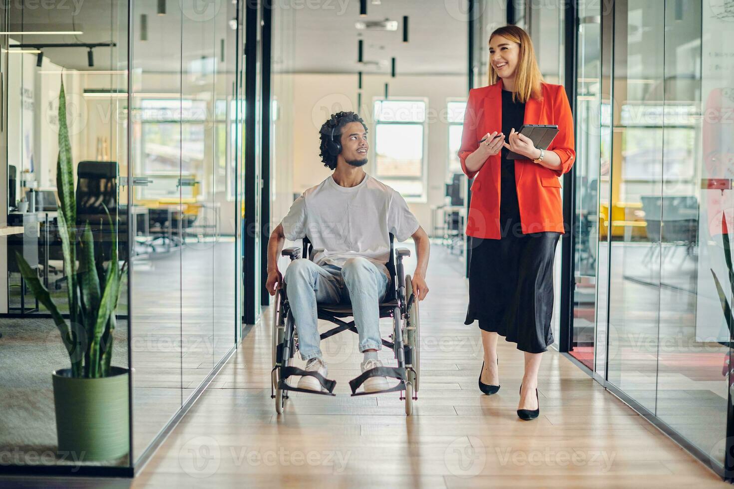 een groep van jong bedrijf mensen in een modern glazen wanden kantoor vangt de essence van verscheidenheid en samenwerking, terwijl twee collega's, inclusief een Afrikaanse Amerikaans zakenman in een rolstoel, reflecteren inclusiviteit en bespreken oplossen bedrijf probleem foto