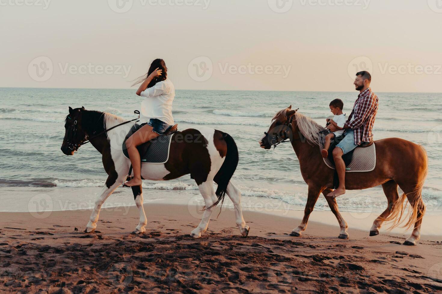 de familie besteedt tijd met hun kinderen terwijl rijden paarden samen Aan een zanderig strand. selectief focus foto