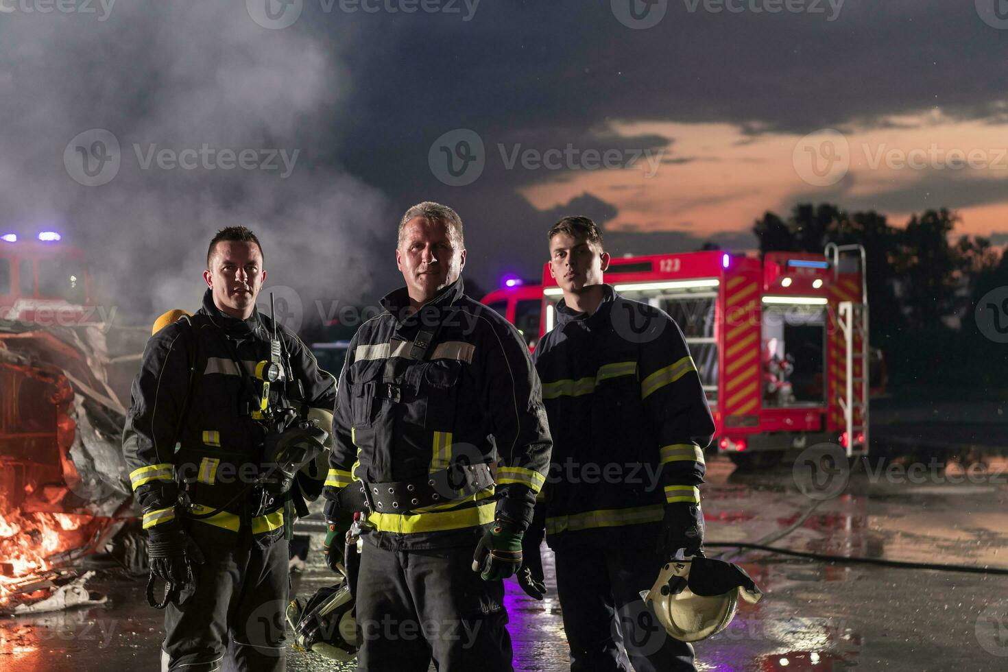 dapper brandweerlieden team wandelen naar de camera. in achtergrond paramedici en brandweer redden team strijd brand in auto ongeluk, verzekering en opslaan volkeren leeft concept. foto