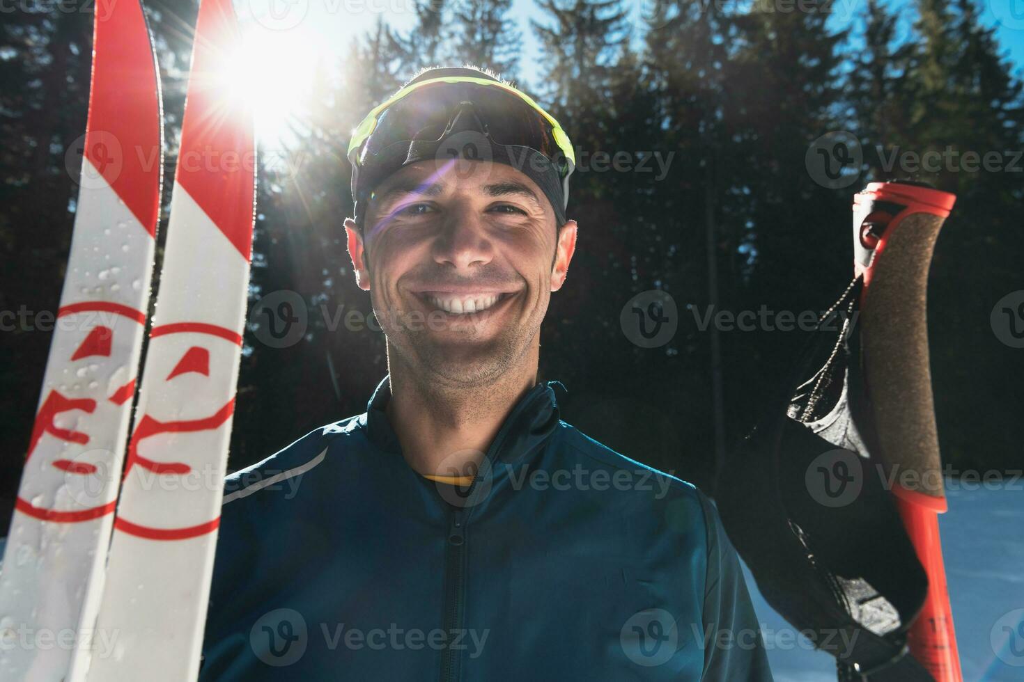 portret knap mannetje atleet met kruis land skis in handen en stofbril, opleiding in besneeuwd Woud. gezond winter levensstijl concept. foto