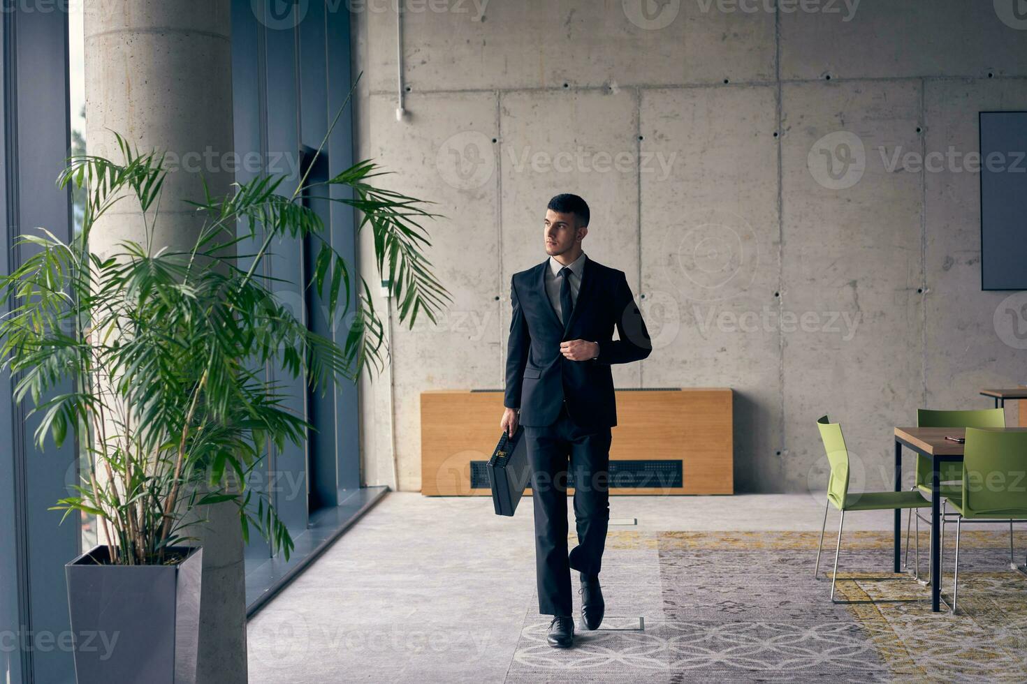 een zelfverzekerd zakenman met een aktentas stappen door een modern kantoor, uitstralend charisma en bepaling, symboliseert succes en professioneel uitmuntendheid. foto