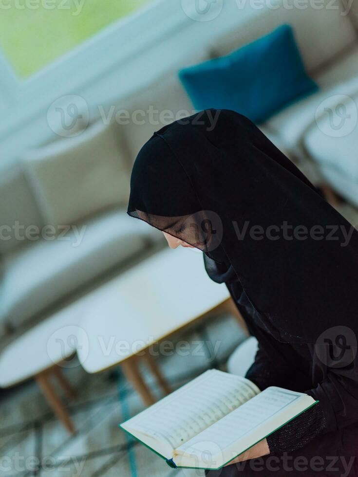 jong traditioneel moslim vrouw lezing koran Aan de sofa voordat iftar avondeten gedurende een Ramadan feest Bij huis foto