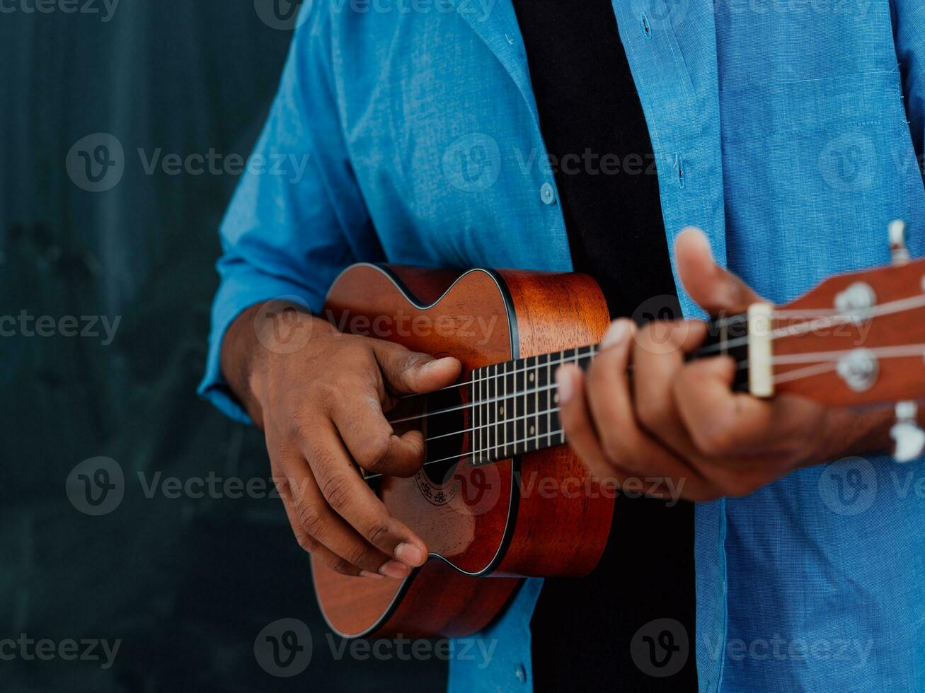 Indisch jong Mens in een blauw overhemd en bril spelen de gitaar in voorkant van de school- schoolbord foto