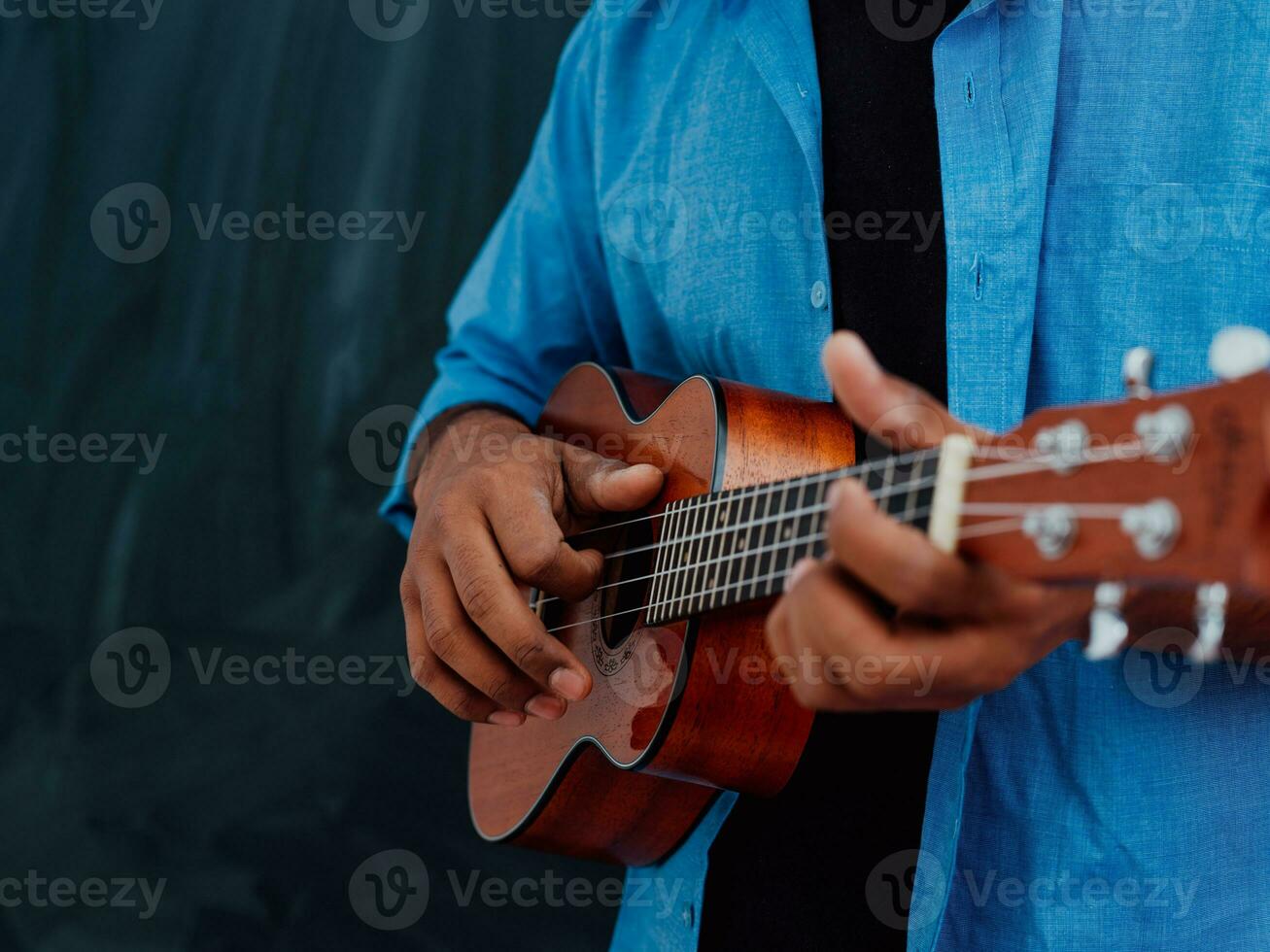 Indisch jong Mens in een blauw overhemd en bril spelen de gitaar in voorkant van de school- schoolbord foto