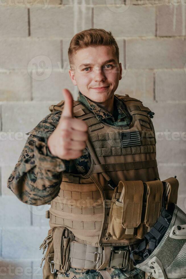 de soldaat maakt een gebaar van succes met zijn hand. een soldaat in vol oorlog uitrusting staat in voorkant van een steen muur en shows de OK teken met zijn vinger foto