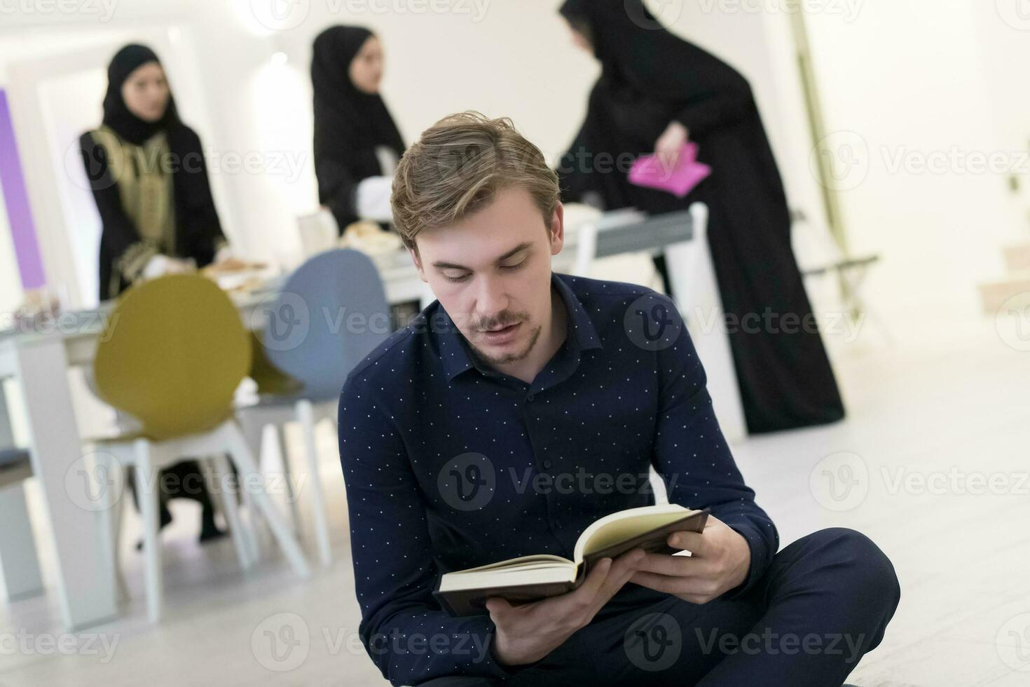 jong moslim Mens zittend Aan de verdieping terwijl lezing heilig boek koran voordat iftar avondeten gedurende een Ramadan feest Bij huis foto