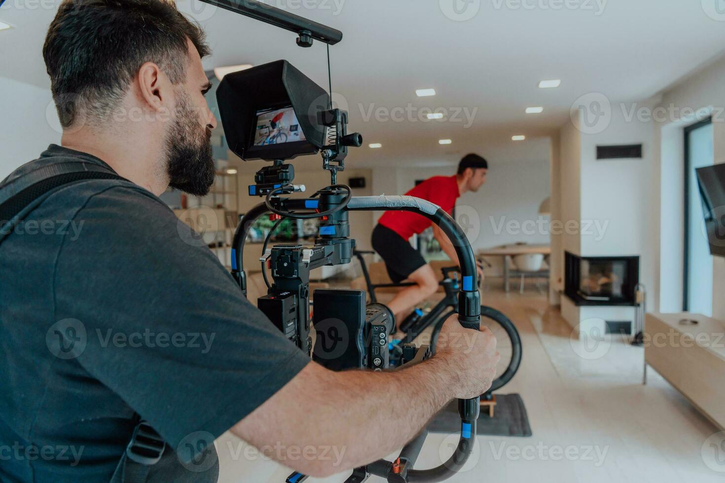 een cameraman filmen een atleet rijden een triatlon fiets Aan een simulatie machine in een modern leven kamer. opleiding in pandemisch conditie. foto