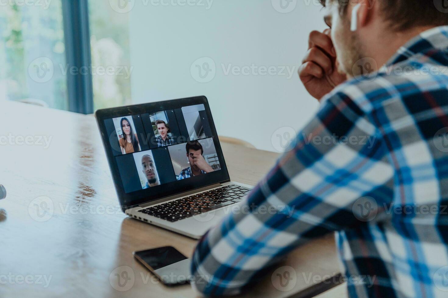 de Mens zittend Bij een tafel in een modern leven kamer, met hoofdtelefoons gebruik makend van een laptop voor bedrijf video chatten, gesprek met vrienden en vermaak foto