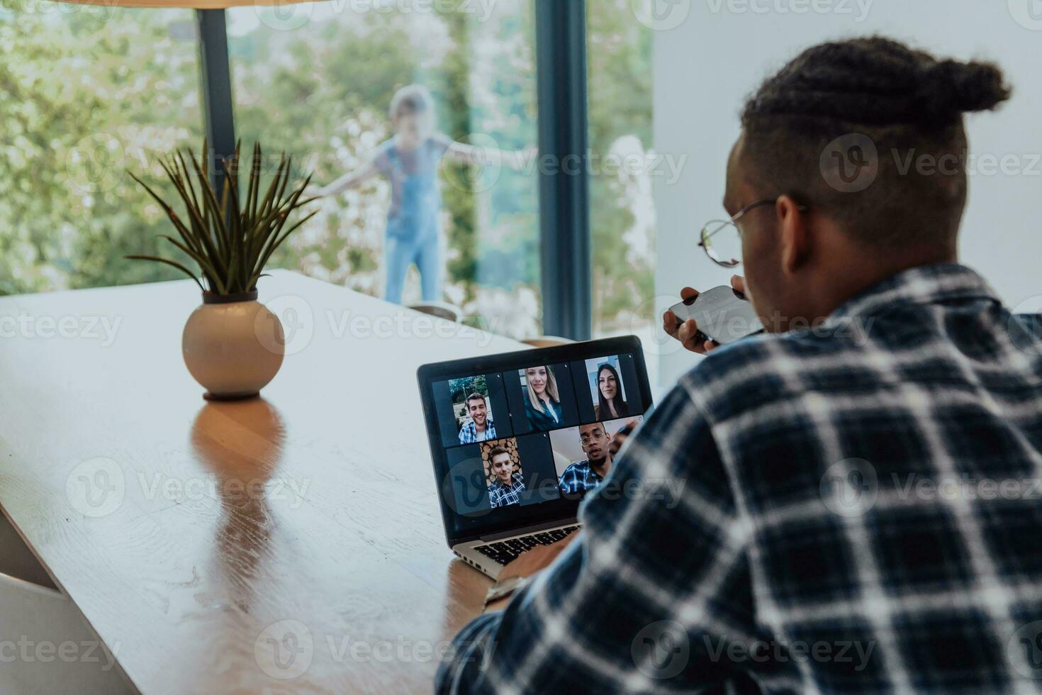 Afrikaanse Amerikaans Mens in bril zittend Bij een tafel in een modern leven kamer, gebruik makend van een laptop en smartphone voor bedrijf video chatten, gesprek met vrienden en vermaak foto