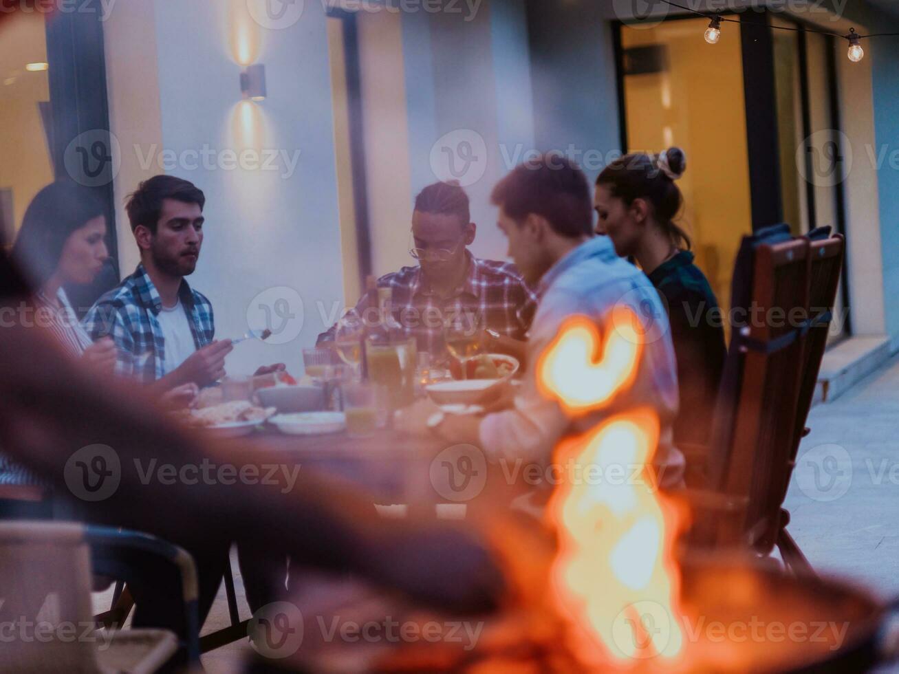 een groep van jong verschillend mensen hebben avondeten Aan de terras van een modern huis in de avond. pret voor vrienden en familie. viering van vakantie, bruiloften met barbecue. foto