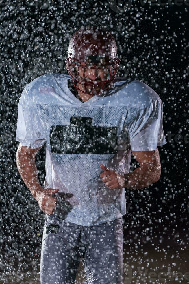 Amerikaans Amerikaans voetbal veld- eenzaam atleet krijger staand Aan een veld- houdt zijn helm en klaar naar Speel. speler voorbereidingen treffen naar rennen, aanval en partituur touchdown. regenachtig nacht met dramatisch mist, blauw licht foto