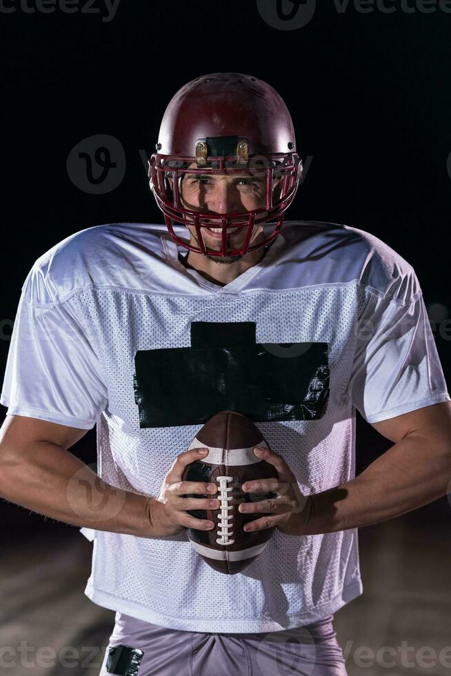 Amerikaans Amerikaans voetbal veld- eenzaam atleet krijger staand Aan een veld- houdt zijn helm en klaar naar Speel. speler voorbereidingen treffen naar rennen, aanval en partituur touchdown. regenachtig nacht met dramatisch mist, blauw licht foto