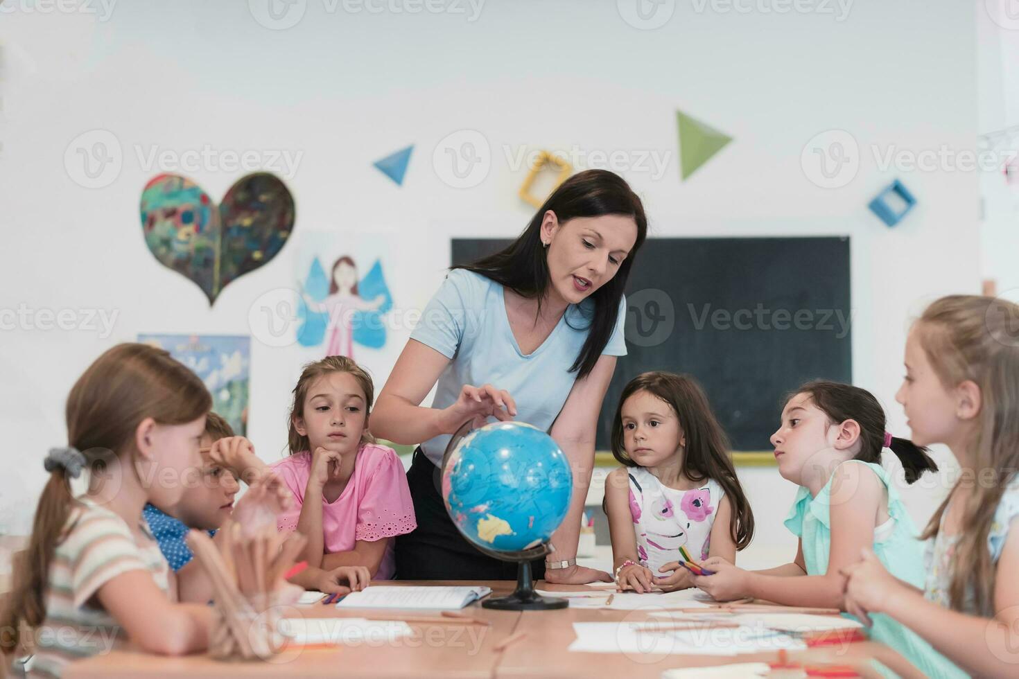 vrouw leraar met kinderen in aardrijkskunde klasse op zoek Bij wereldbol. kant visie van groep van verschillend gelukkig school- kinderen met wereldbol in klas Bij school. foto