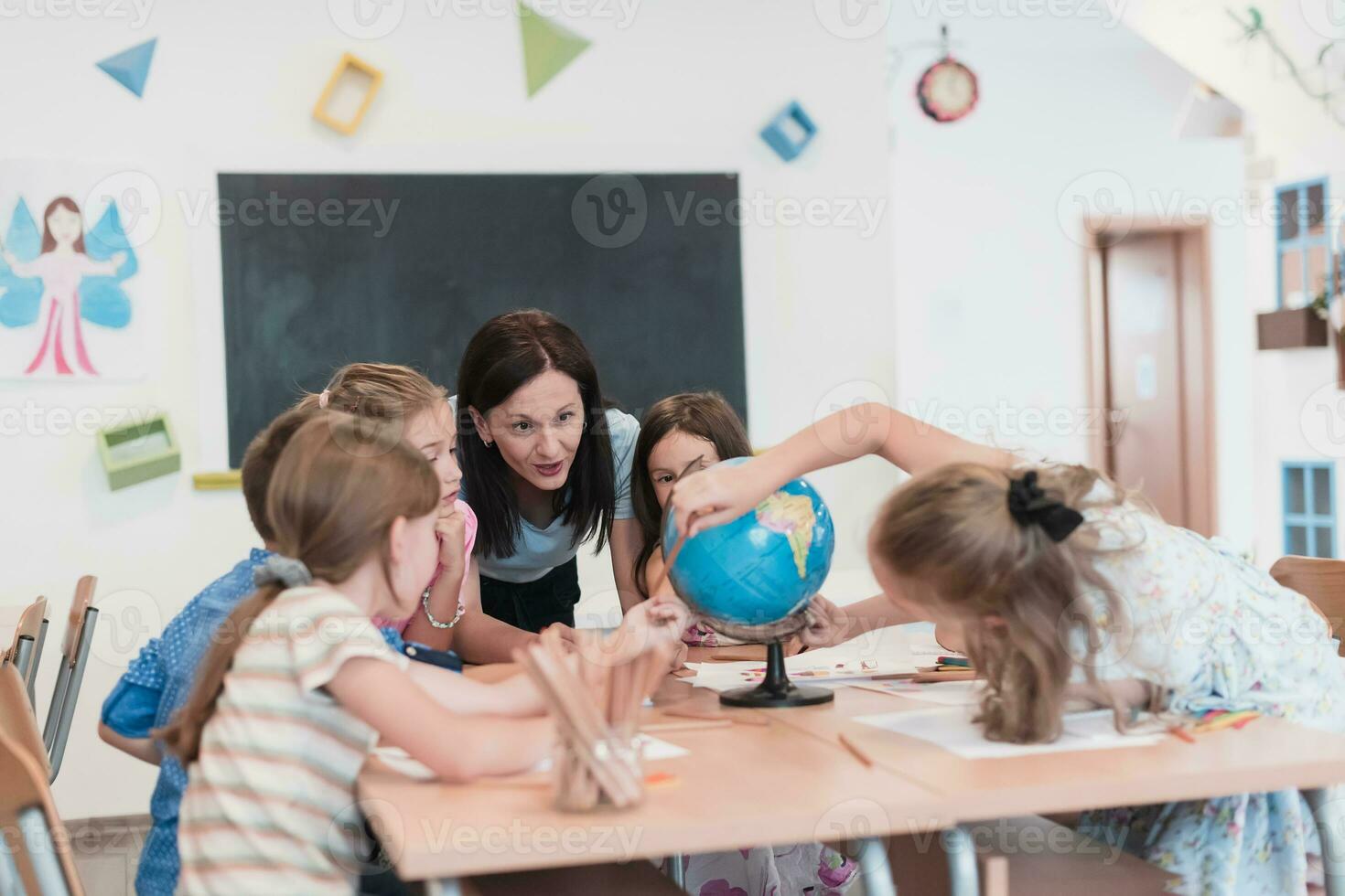 vrouw leraar met kinderen in aardrijkskunde klasse op zoek Bij wereldbol. kant visie van groep van verschillend gelukkig school- kinderen met wereldbol in klas Bij school. foto