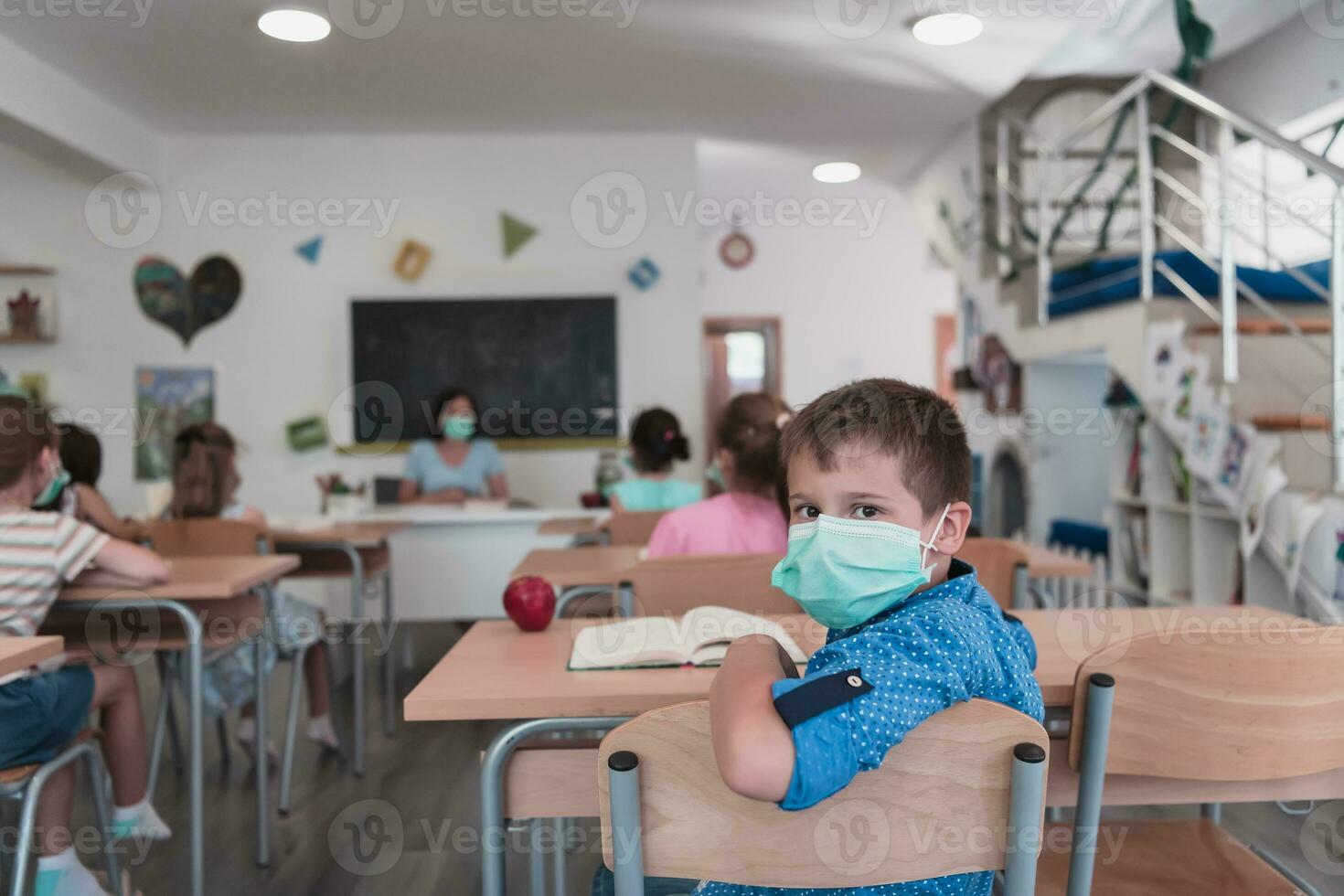 multiraciaal groep van kinderen vervelend gezicht maskers werken Bij klas, schrijven en luisteren uitleg van leraar in klas foto