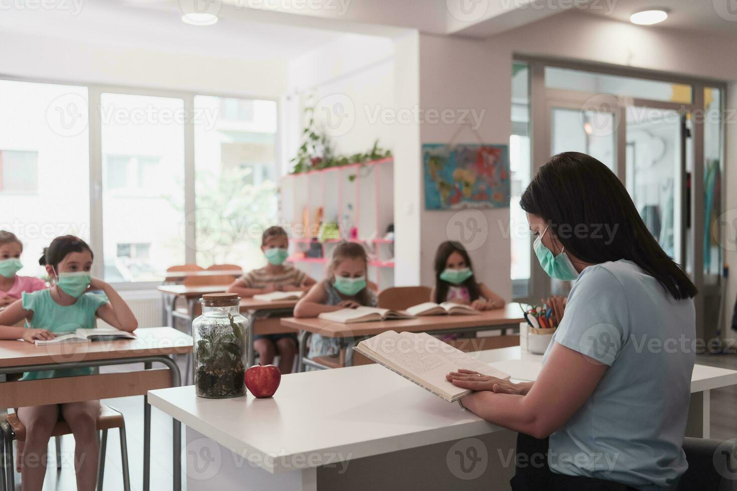 multiraciaal groep van kinderen vervelend gezicht maskers werken Bij klas, schrijven en luisteren uitleg van leraar in klas foto