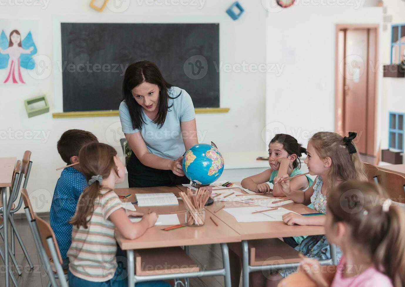 vrouw leraar met kinderen in aardrijkskunde klasse op zoek Bij wereldbol. kant visie van groep van verschillend gelukkig school- kinderen met wereldbol in klas Bij school. foto