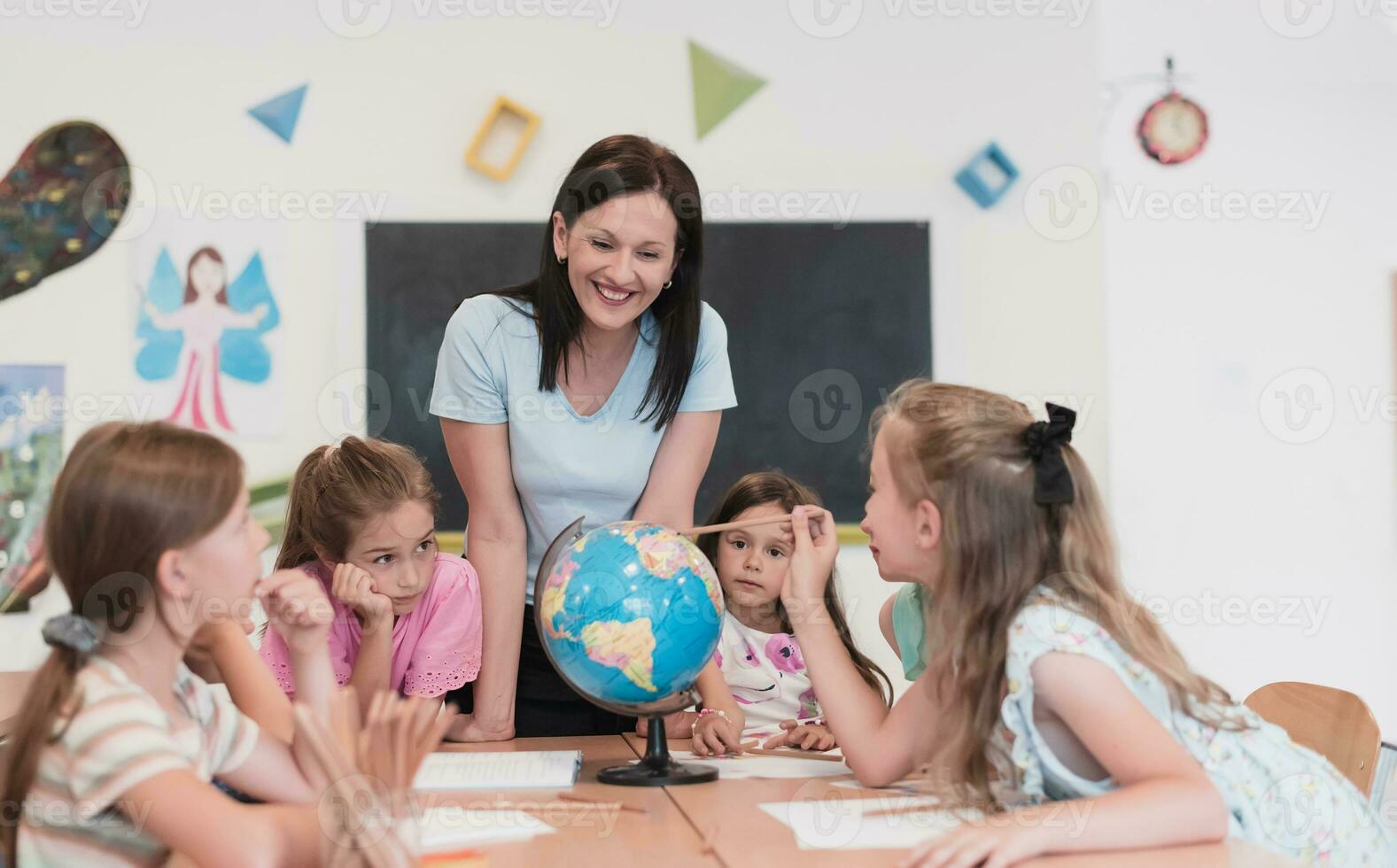 vrouw leraar met kinderen in aardrijkskunde klasse op zoek Bij wereldbol. kant visie van groep van verschillend gelukkig school- kinderen met wereldbol in klas Bij school. foto