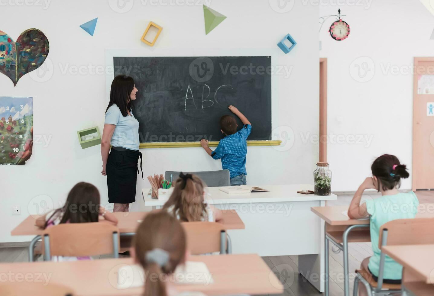 elementair school. de vrouw leraar helpen de kind leerling terwijl schrijven de antwoord Aan de schoolbord. foto