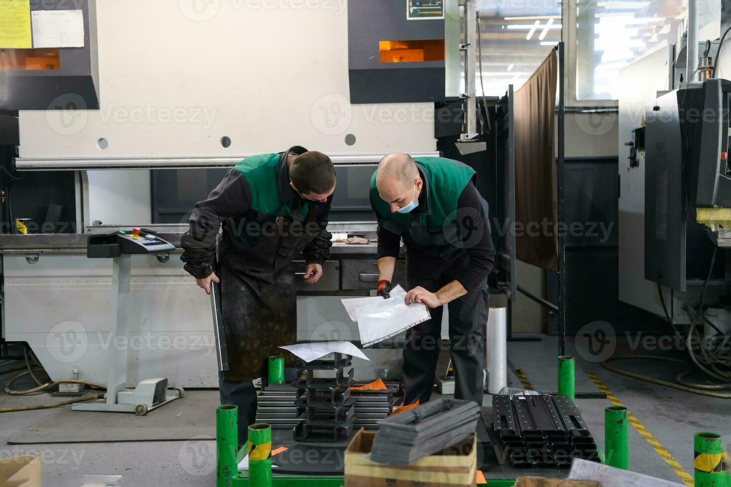 twee arbeiders vervelend een beschermend masker ten gevolge naar een coronavirus pandemie, werken in een modern fabriek en voorbereidingen treffen een programma en materialen voor een cnc machine foto