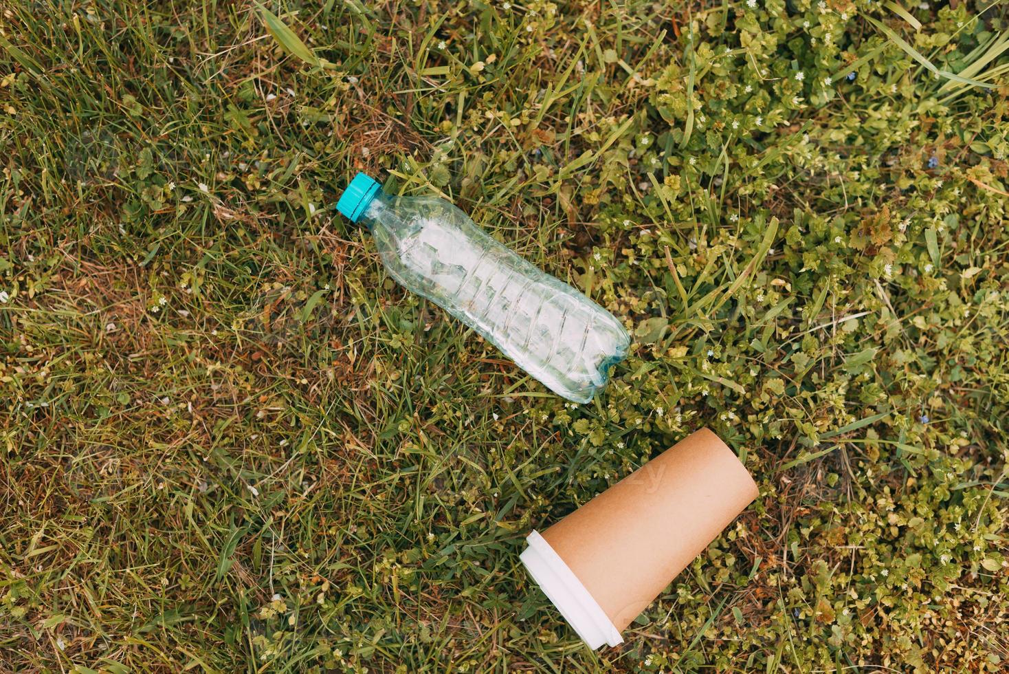 plastic fles en papieren koffiekopje op groen gras, afvalconcept foto