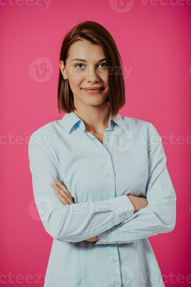 portret schot van een mooi blond zakenvrouw staand met armen gekruiste Bij geïsoleerd roze achtergrond. foto