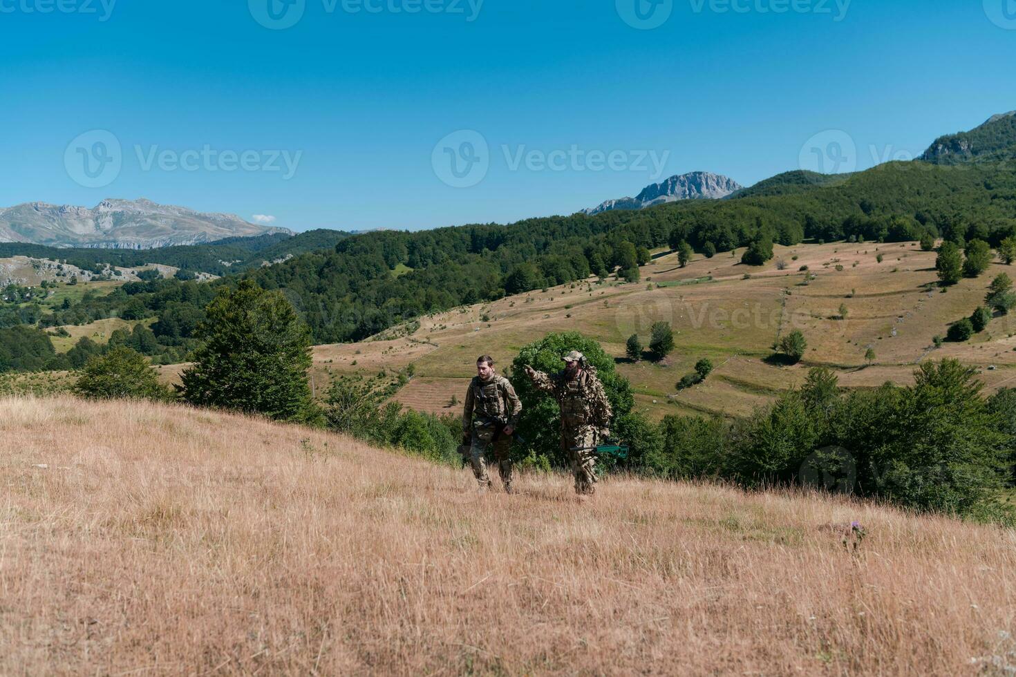 een scherpschutter team ploeg van soldaten is gaan undercover. scherpschutter assistent en team leider wandelen en het richten in natuur met geel gras en blauw lucht. tactisch camouflage uniform. foto
