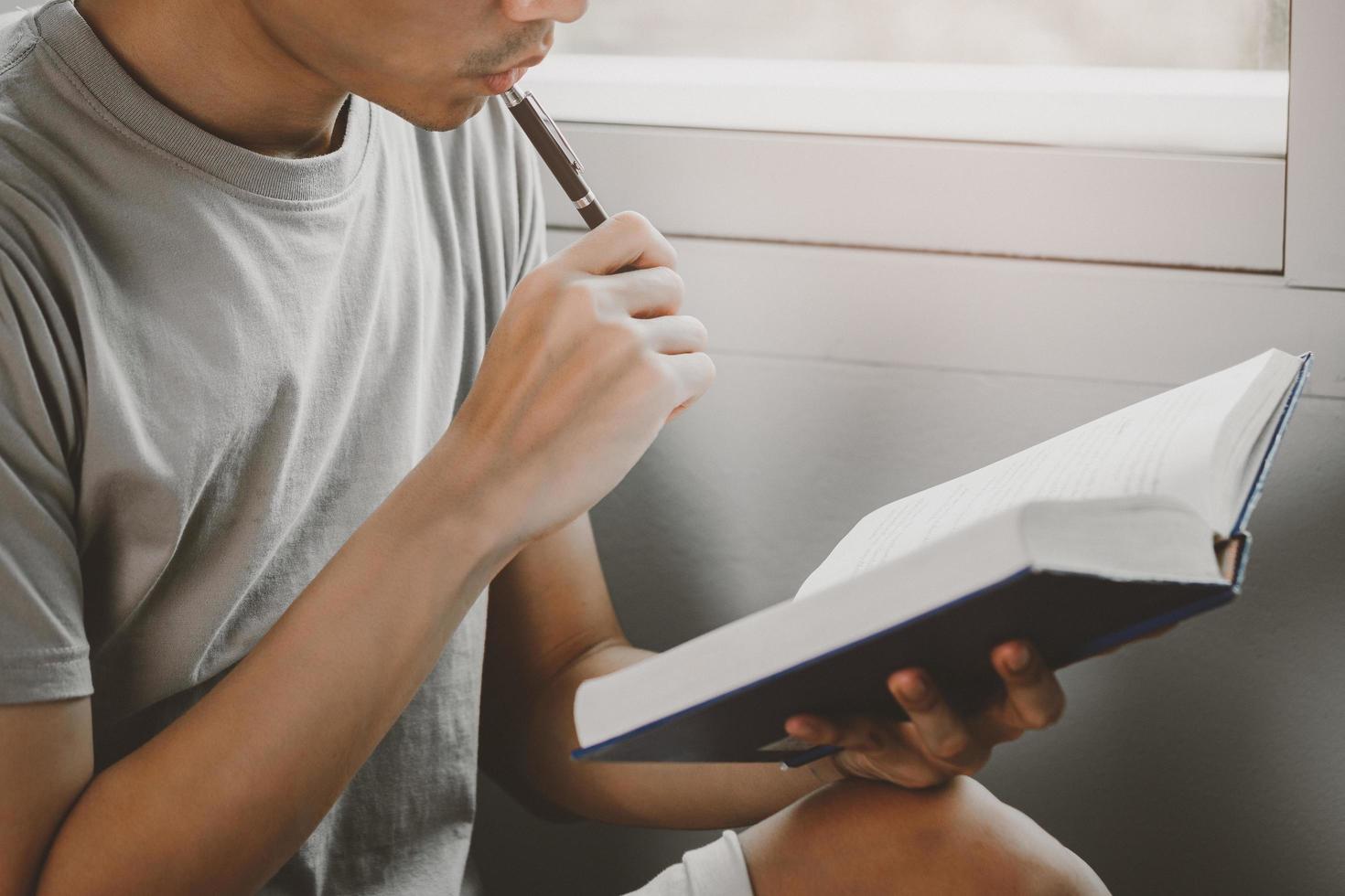 jonge man leesboek en denkend gebaar in de woonkamer foto