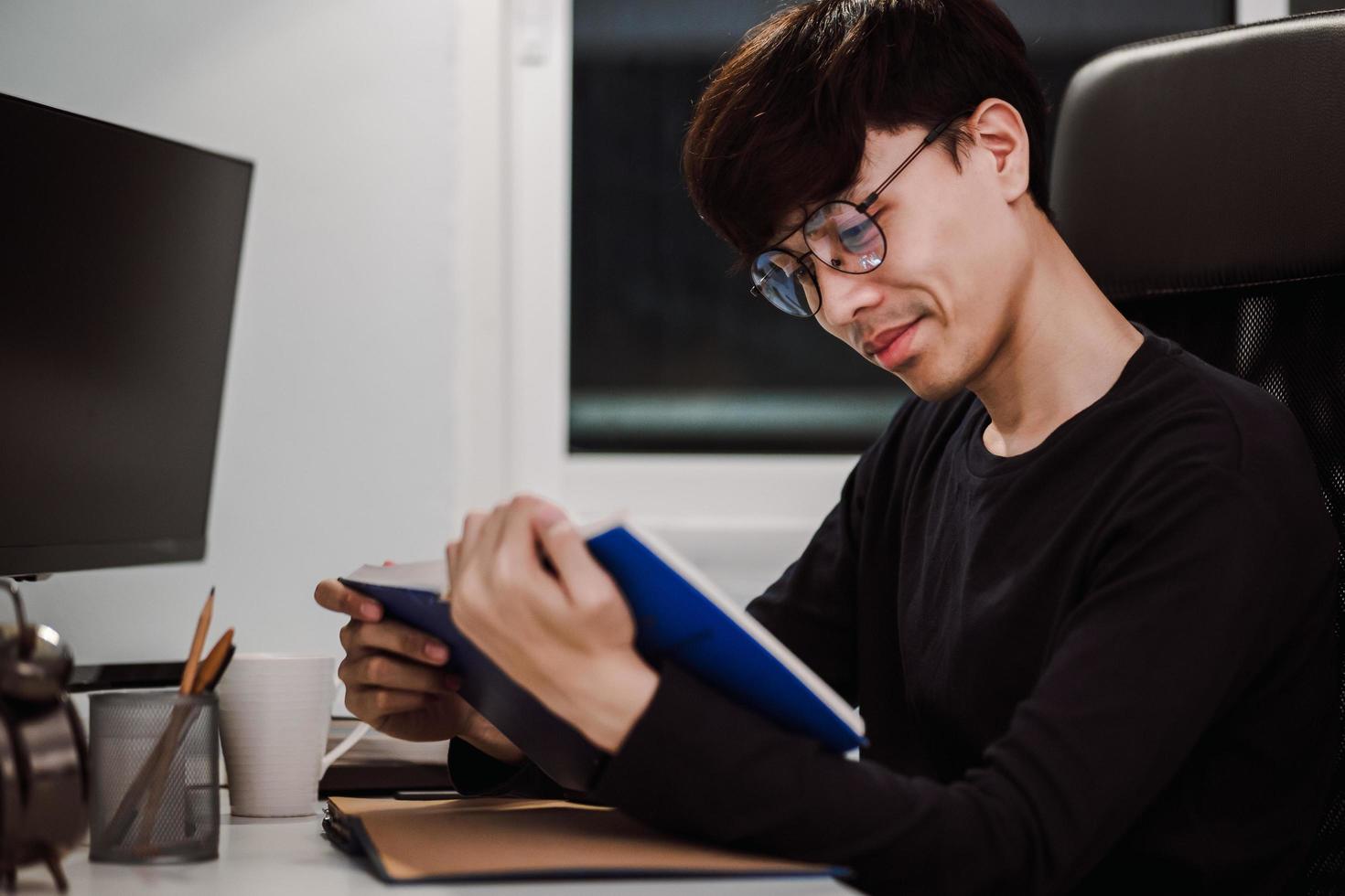 jonge knappe aziatische man die 's avonds laat een boek leest op het bureau foto