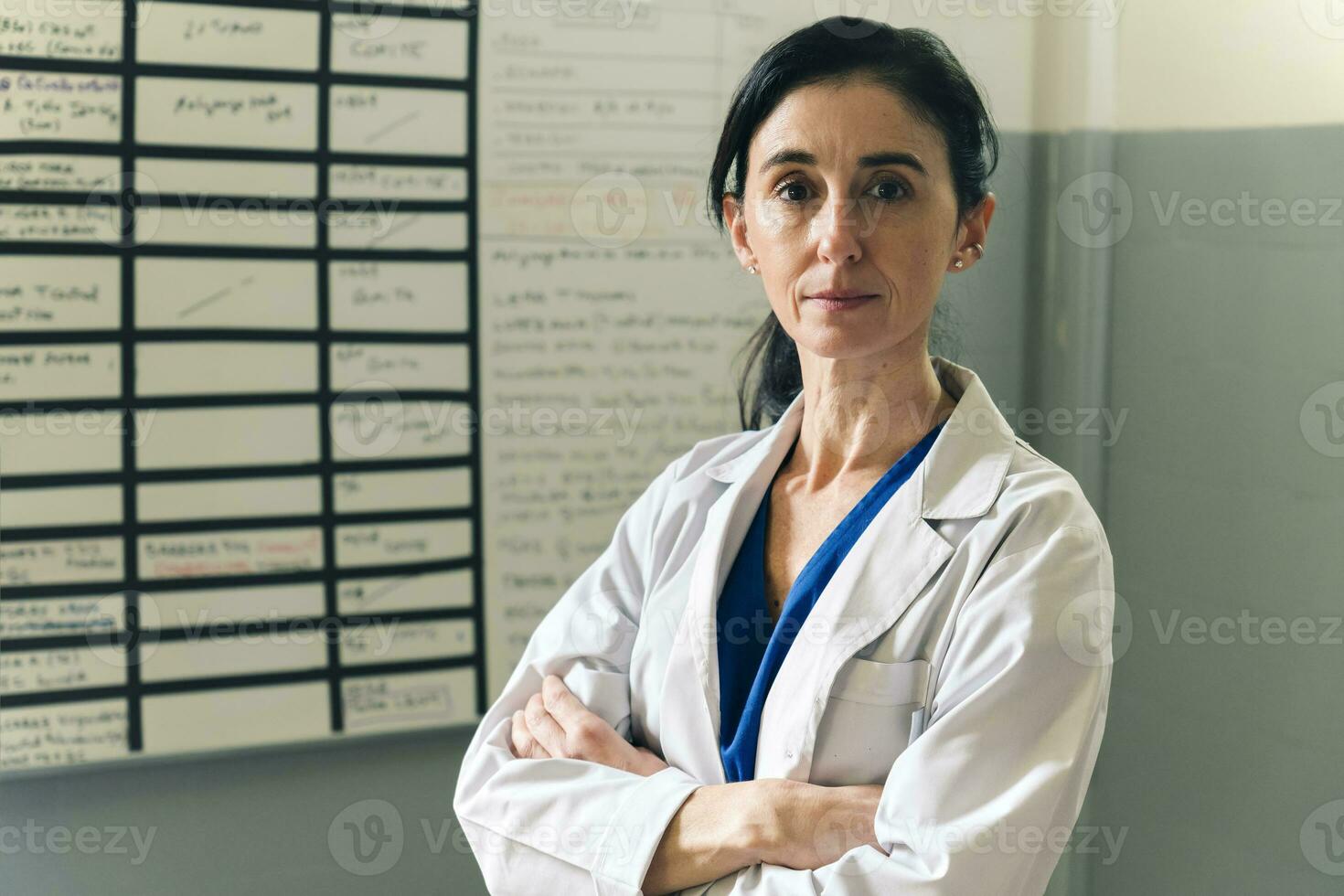 portret van volwassen vrouw dokter op zoek Bij camera met armen gekruiste in kantoor foto