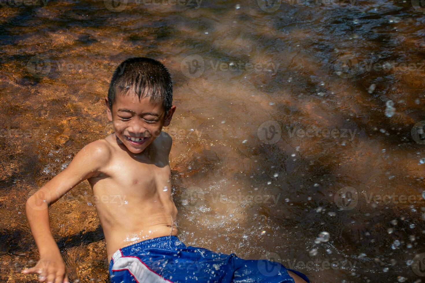 Aziatisch jong jongen schattig glimlachen en charmant spelen water in rivier- Aan achtergrond water oppervlakte en zonsopgangen, kind spelen water, levensstijl van Aziatisch kinderen, begrip van leven en duurzaamheid. foto