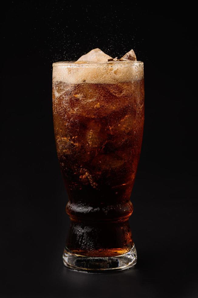 cola in glas met heldere ijsblokjes geïsoleerd op zwarte achtergrond foto