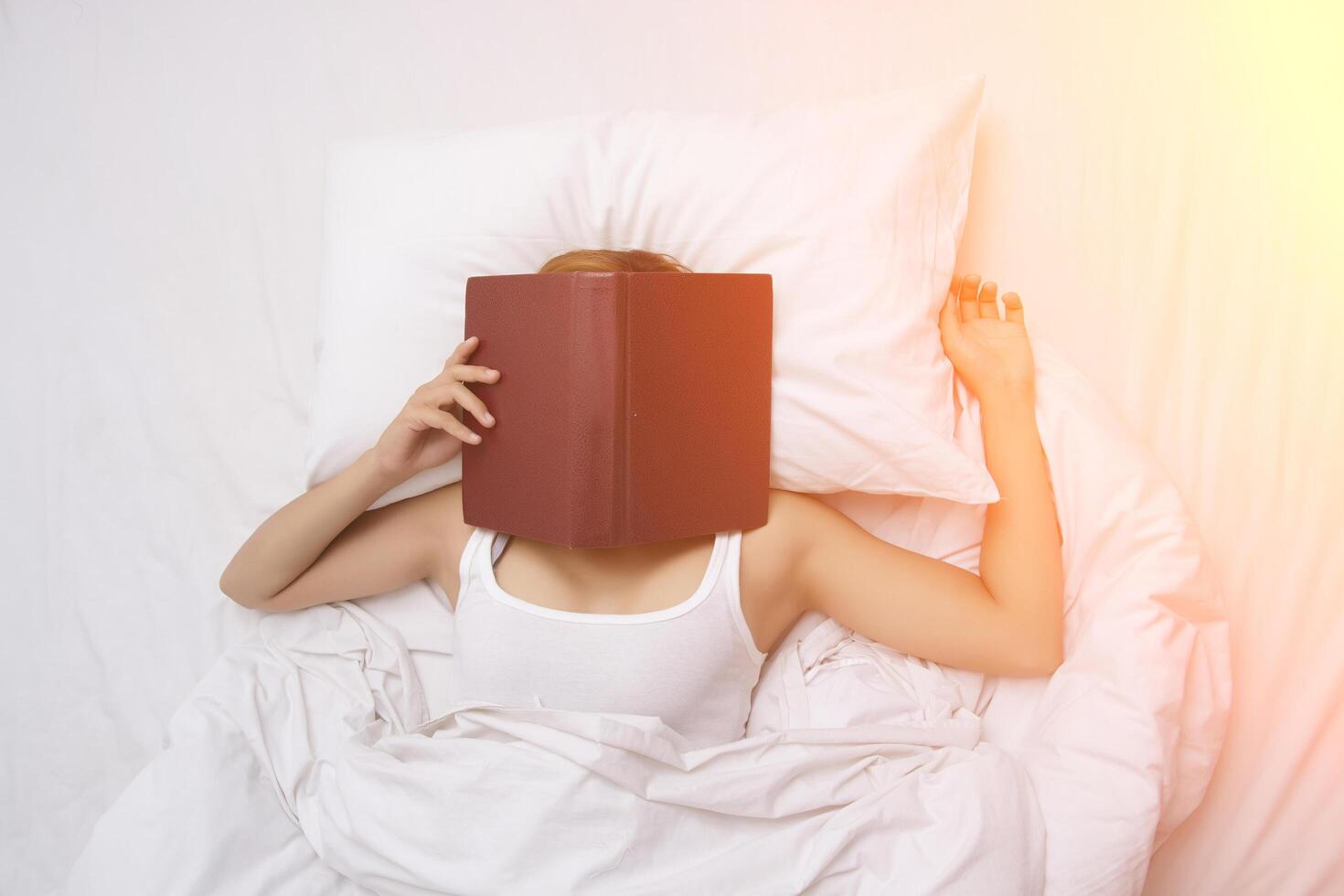 jonge vrouw slapen op het bed na met gezicht bedekt door het boek. foto