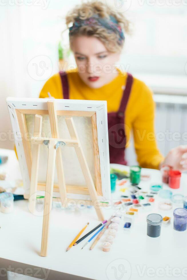 vrouw zittend in voorkant van een schilderij en schilderij met borstels Aan canvas Bij huis foto