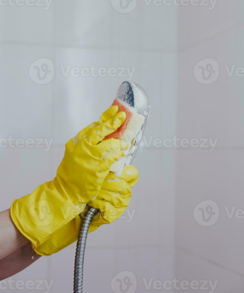 vrouw in rubber handschoenen schoonmaak de douche hoofd. dienstmeisje het wassen metalen hoofd van de douche. huisvrouw schoonmaak omhoog in de badkamer foto