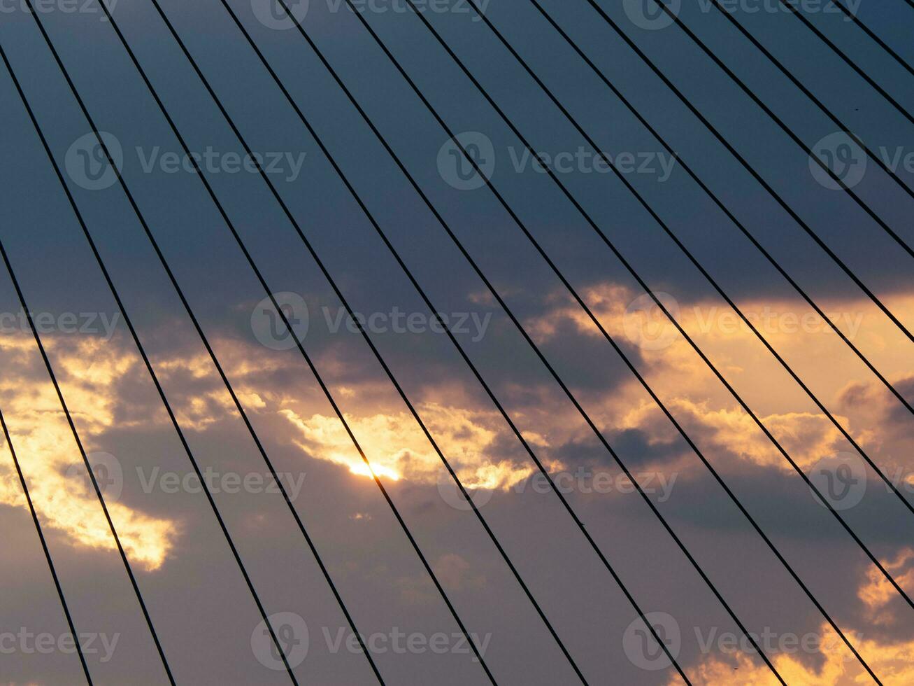 zonsondergang achter de wolken gezien door de kabels van de suspensie brug foto