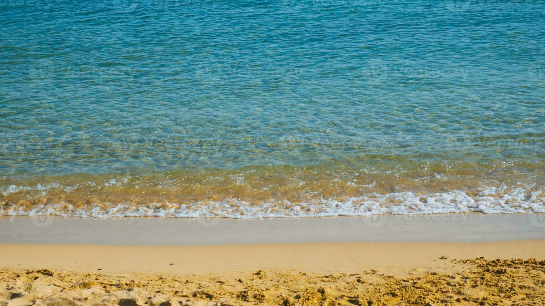 zanderig strand met klein golven - blauw zee en geel zand foto