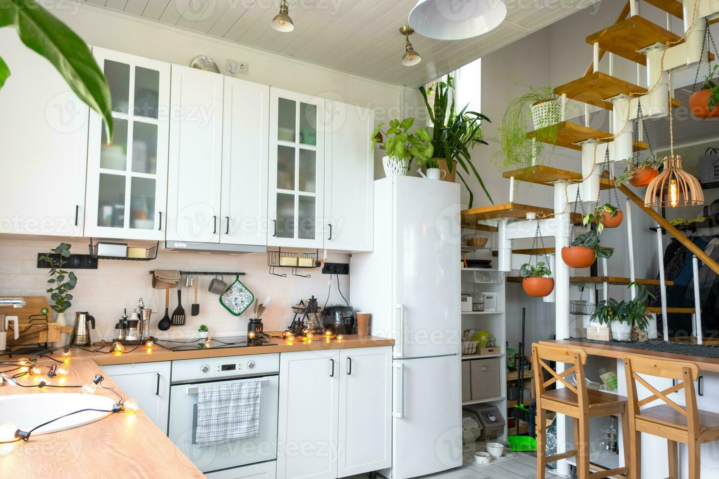 de algemeen plan van een licht wit modern rustiek keuken met een modulair metaal trappenhuis versierd met ingemaakt planten. interieur van een huis met thuisplanten foto