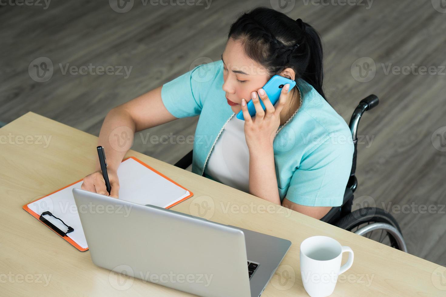 Aziatische gehandicapte vrouw die in een rolstoel zit en op kantoor werkt foto