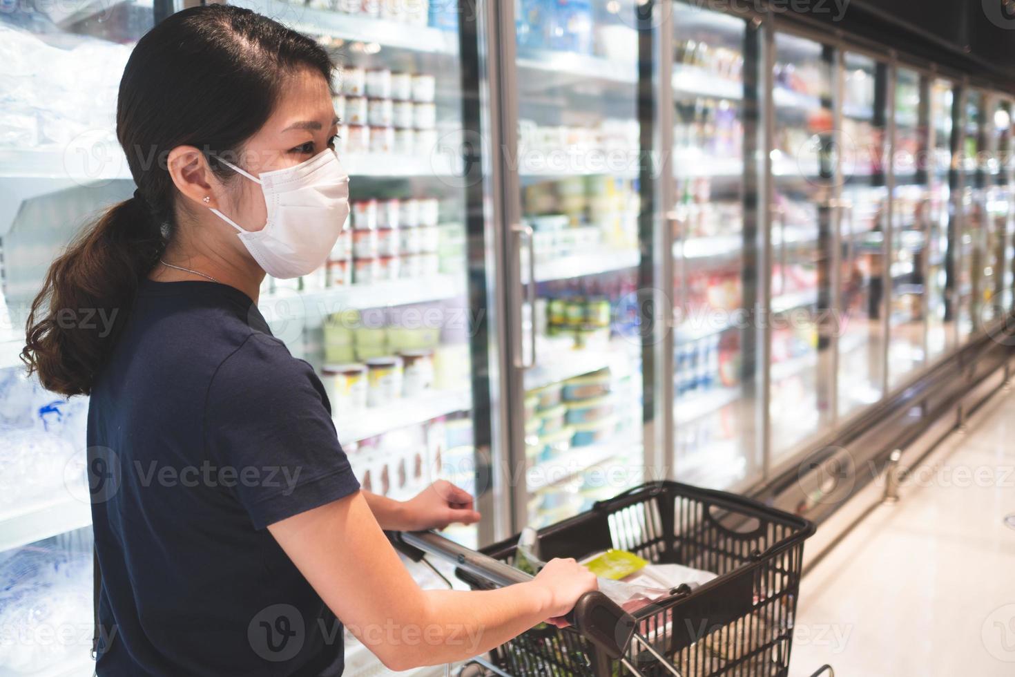 jonge aziatische vrouw die een masker draagt tijdens het winkelen in de supermarkt foto