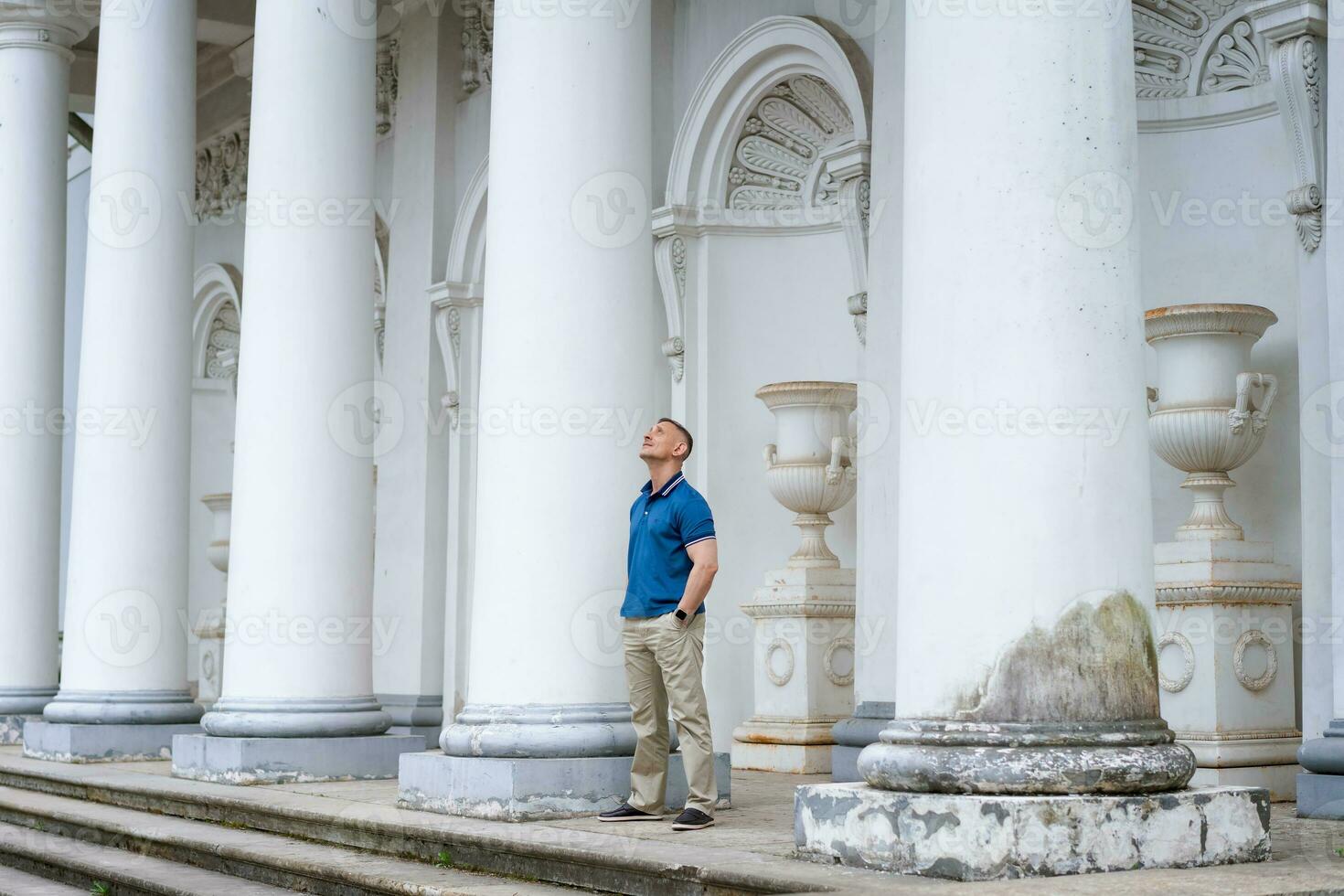 een Mens in gewoontjes kleren staat in de buurt de kolommen van een wit gebouw foto