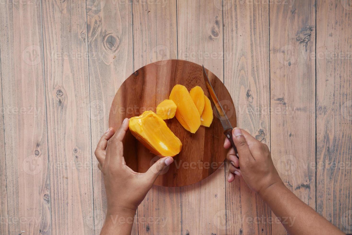 bovenaanzicht van jonge man hand snijden mango op snijplank foto
