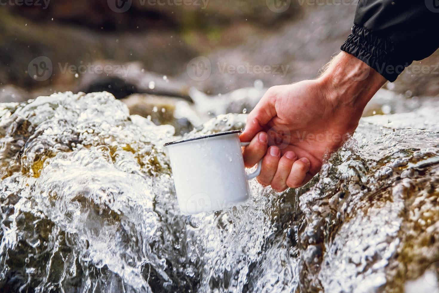 iemands hand houdt een metalen mok vast tegen de achtergrond van de rivier foto